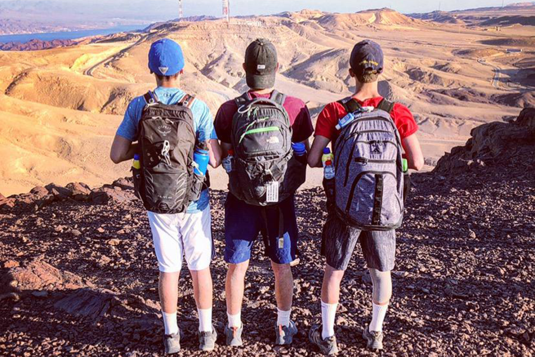 three campers with their back towards the camera looking over a view of mountains